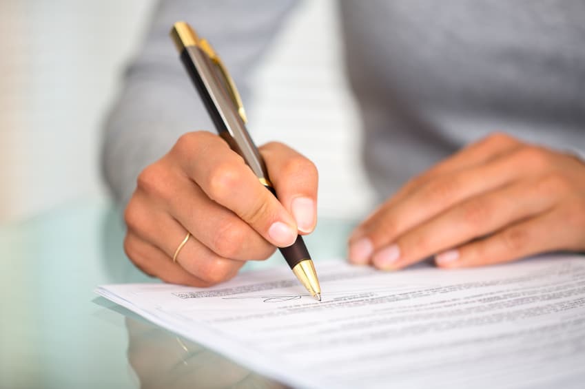 Woman at office desk signing a contract with shallow focus on si