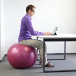 une homme travaille sur ordinateur assis sur une boule